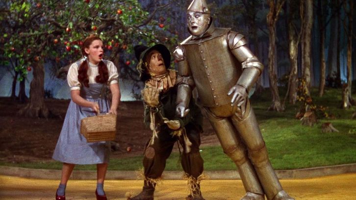 Film still from THE WIZARD OF OZ: Dorothy, the Scarecrow and Tin Man on a path.