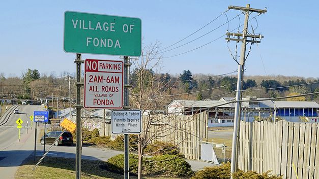 Film still from "Henry Fonda for President " by Alexander Horwath. It shows the entrance sign to the village of Fonda. A road and houses can be seen in the background. 