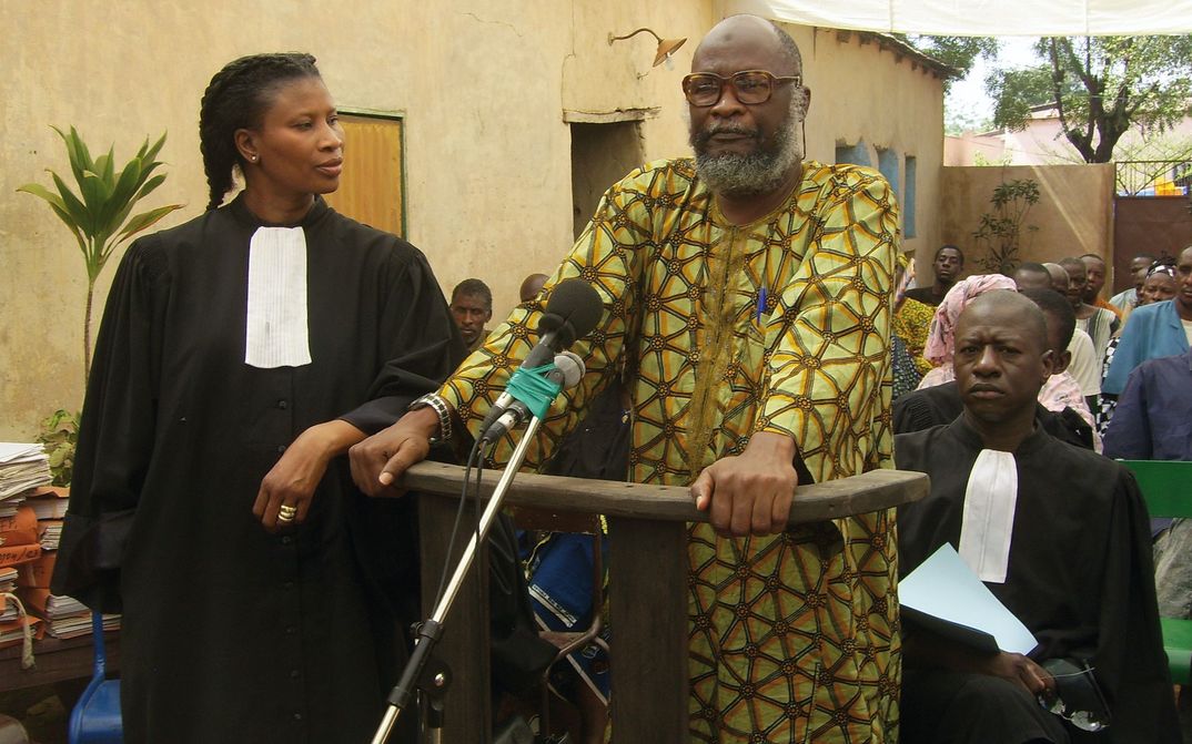 Film still from BAMAKO: An improvised courtroom scene in the open air. In the foreground a woman in a judge