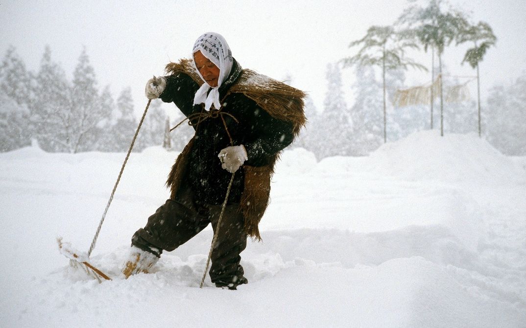 Film still from UNTER SCHNEE: A person in a historical costume is walking through a snow-covered landscape on snowshoes.