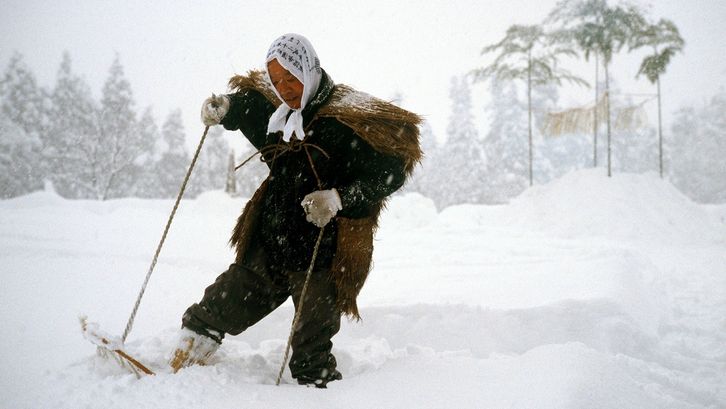 Filmstill aus UNTER SCHNEE: Eine Person in einem historischen Kostüm läuft mit Schneeschuhen durch eine verschneite Landschaft.