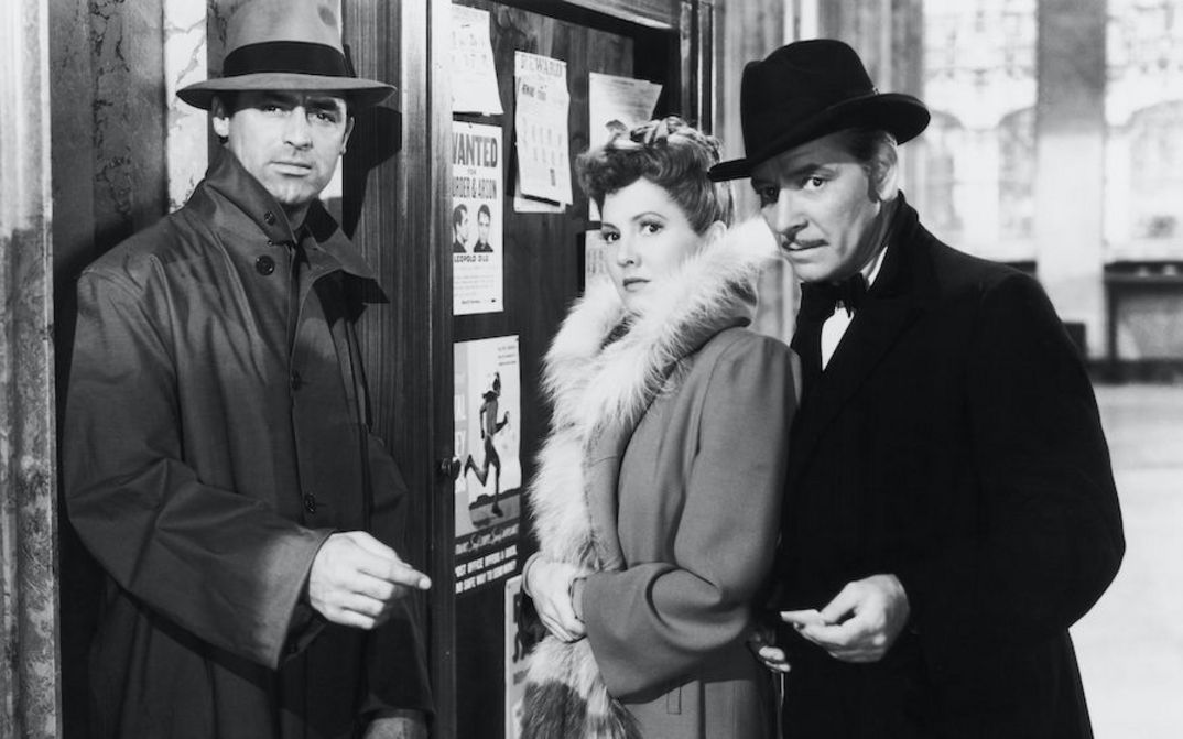 Filmstill aus THE TALK OF THE TOWN: Eine Frau steht zwischen zwei Männern. Alle sind gut gekleidet und blicken in die gleiche Richtung.