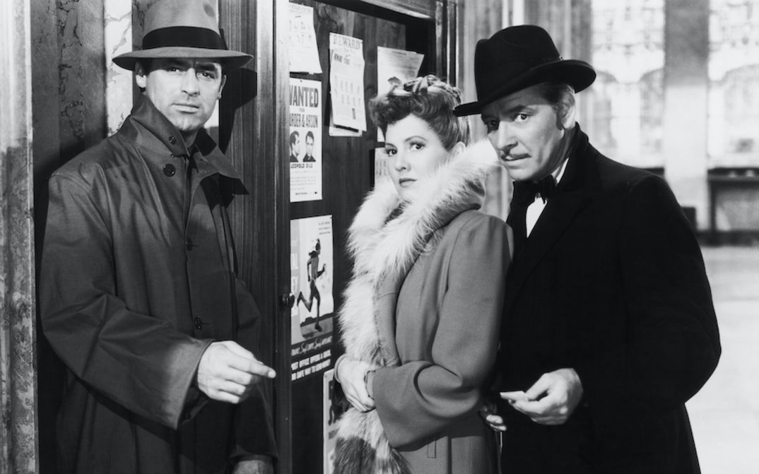 Film still from THE TALK OF THE TOWN: A woman stands between two men. They are all well dressed and looking in the same direction.