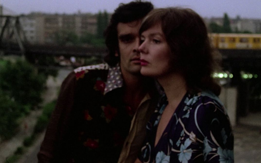 Film still from ERZÄHLEN. The faces of a man and a woman half uperimposed. In the background the elevated railroad.