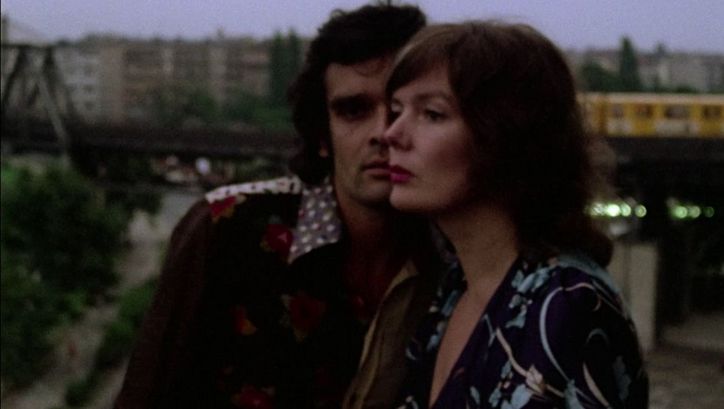 Filmstill aus ERZÄHLEN. Die Gesichter eines Mannes und einer Frau halb übereinander. Im Hintergrund die Berliner Hochbahn.