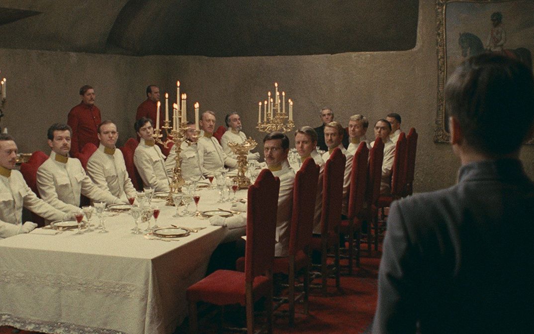 Filmstill aus Il deserto dei tartari: An einer langen, edel gedeckten Tafel sitzen Offiziere in weißen Uniformen. Alle blicken in eine Ecke, in der ein jüngerer Mann steht.