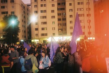 35-mm-Farbfoto. Eine Menschenmenge hat sich zu einer abendlichen Demonstration versammelt, viele von ihnen tragen große lila Fahnen. Am rechten Rand hat die Aufnahme ein rotes Lichtleck.