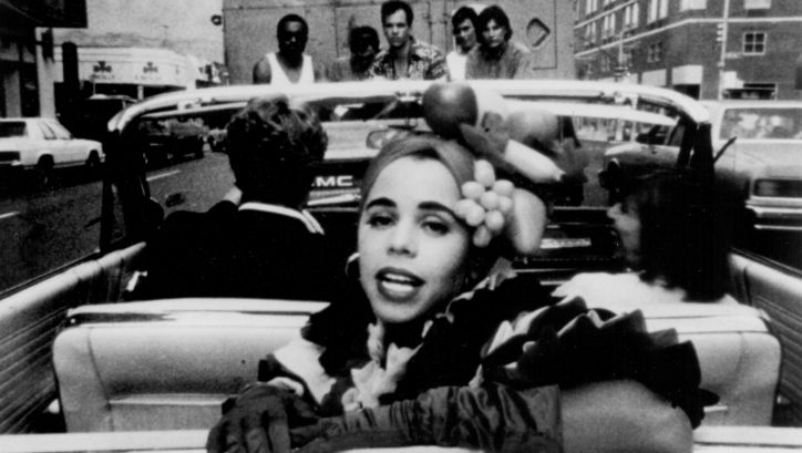 Filmstill aus PRIVILEGE: Eine Frau dreht sich auf dem Rücksitz eines Cabrios zum Betrachter um.