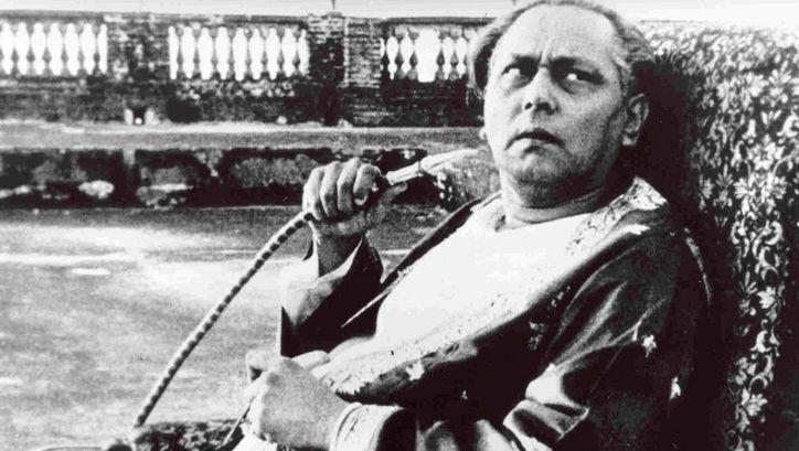 Filmstill from JALSAGHAR: An older man sits on an armchair, looks up sceptically and holds a shisha hose in his hand.