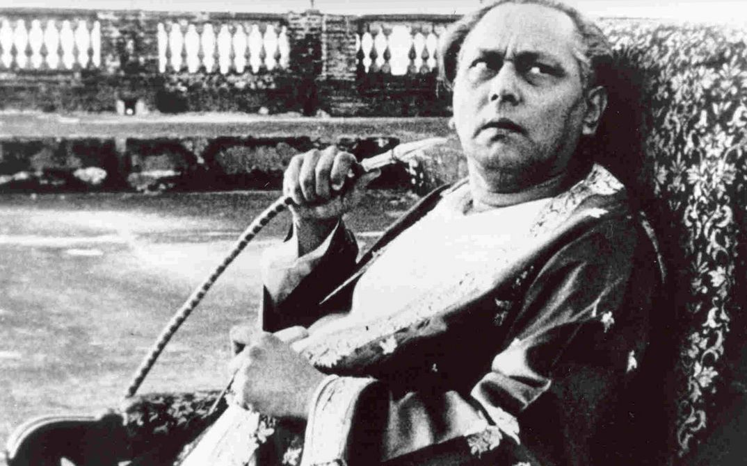 Filmstill from JALSAGHAR: An older man sits on an armchair, looks up sceptically and holds a shisha hose in his hand.