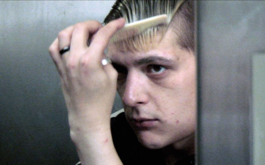 Film still from DRIFTER. A young man combs his hair in front of a mirror.
