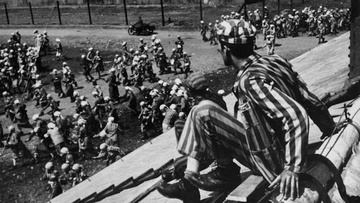 Film still from THE END OF OUR WORLD: A scene in a concentration camp, a prisoner sits on the roof of a barrack.