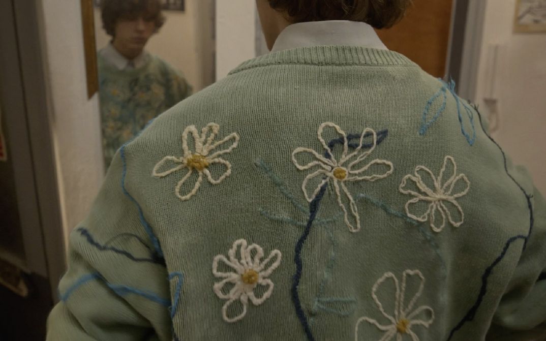 Film still from THE SWAN SONG OF FEDOR OZEROV by Yuri Semashko.The image shows the back of a man wearing a light green sweater embroidered with flowers.