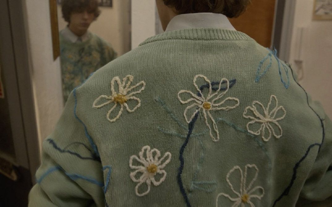 Film still from THE SWAN SONG OF FEDOR OZEROV by Yuri Semashko.The image shows the back of a man wearing a light green sweater embroidered with flowers.