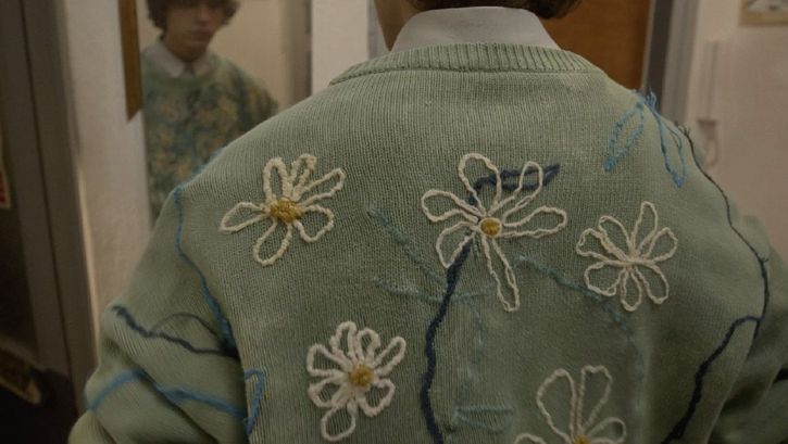 Film still from THE SWAN SONG OF FEDOR OZEROV by Yuri Semashko.The image shows the back of a man wearing a light green sweater embroidered with flowers.