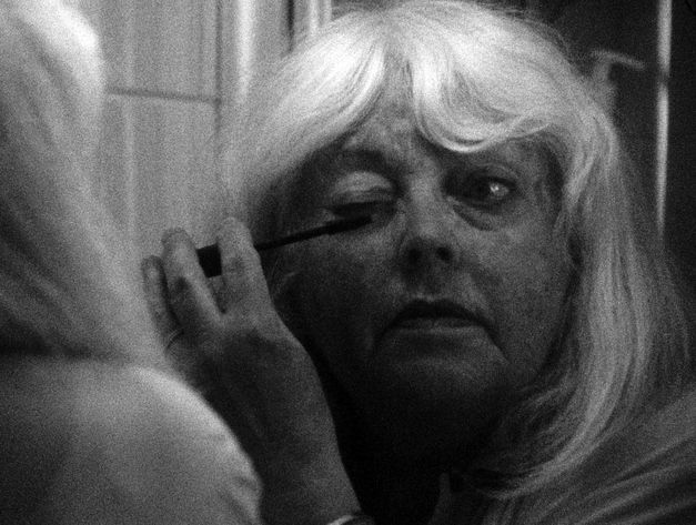 Frau steht vor einem Spiegel und trägt mit einer Bürste oder einem Stift Augen-Make-up auf.