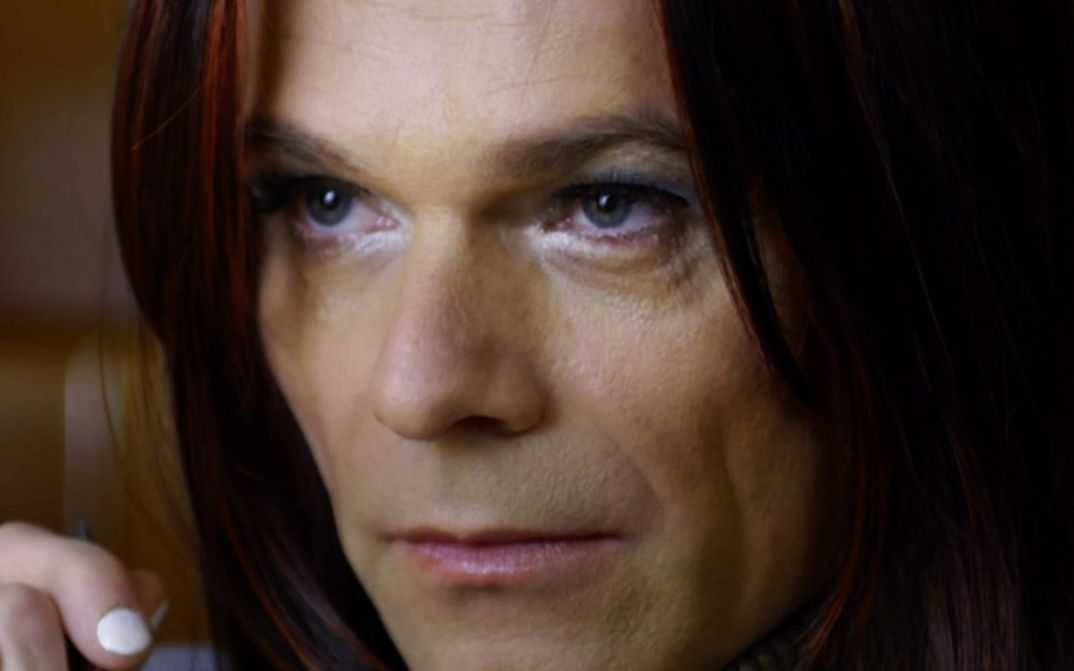 Film still from JANINE ZIEHT AUFS LAND by Jan Eilhardt. The photo shows a close-up of a made-up female face with a serious expression.