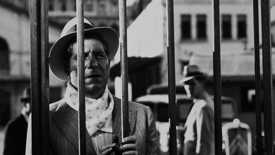 Film still from PÉPÉ LE MOKO: A man is looking through a wire fence.