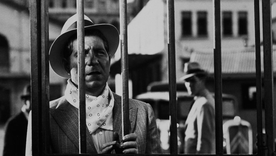Filmstill aus PÉPÉ LE MOKO: Ein Mann schaut durch einen Gitterzaun.
