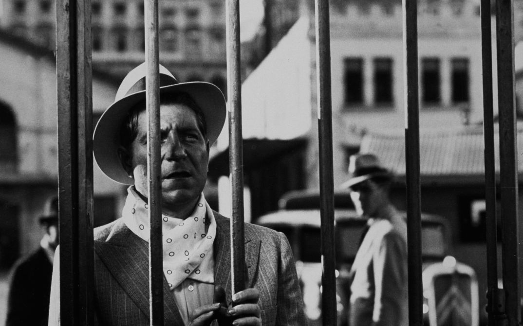 Filmstill aus PÉPÉ LE MOKO: Ein Mann schaut durch einen Gitterzaun.