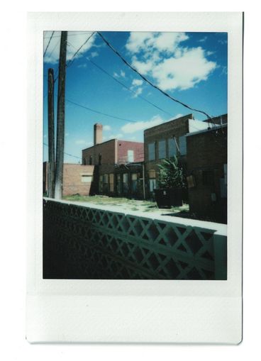 Polaroid of two-floors homes seen from behind a concrete barrier. 