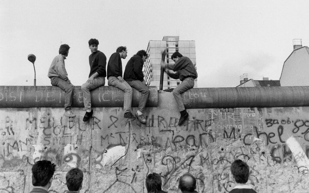 Filmstill aus COUNTDOWN: Einige Menschen sitzen auf der bemalten Berliner Mauer.