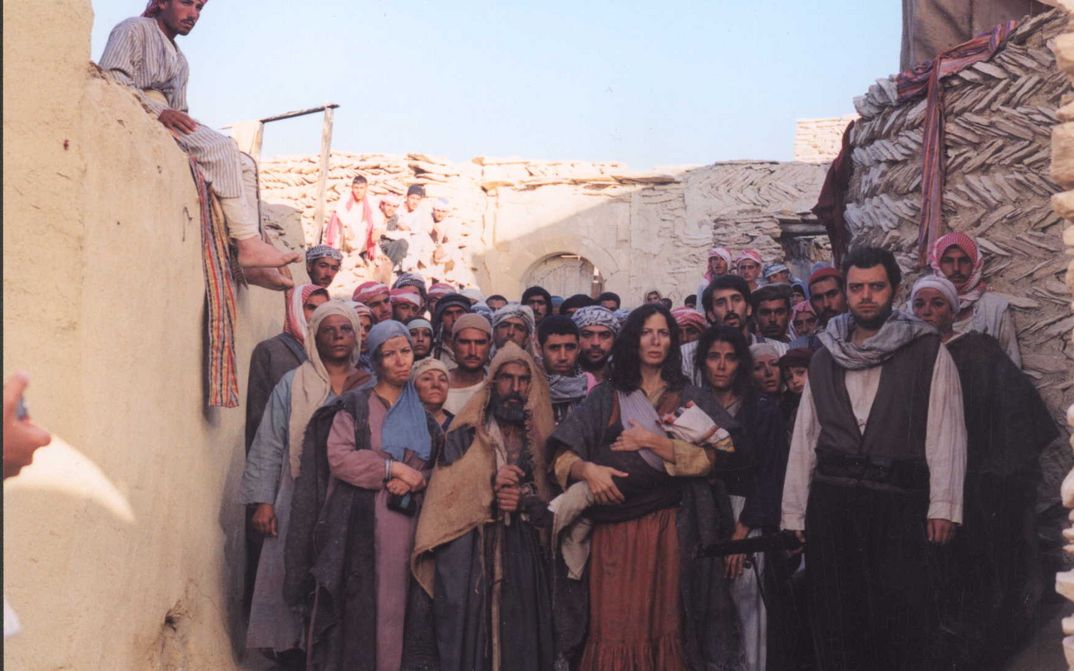 Film still from THE GATE OF SUN: A group of people stand crowded together in an alleyway between houses, gazing into the distance.