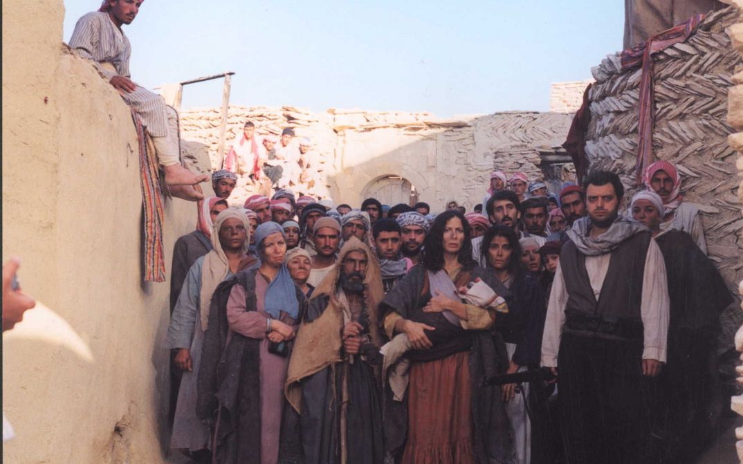 Film still from THE GATE OF SUN: A group of people stand crowded together in an alleyway between houses, gazing into the distance.