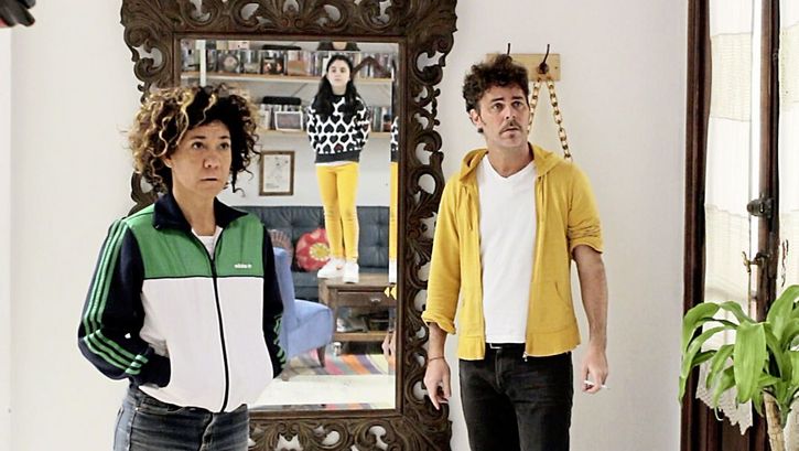 Still from the film "La edad media (The Middle Ages)" by Alejo Moguillansky and Luciana Acuña. A man and a woman stand next to each other in a living room, in the mirror behind them we see the reflection of their daughter standing on a coffee table. 