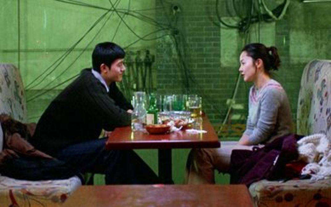 Filmstill aus TALE OF CINEMA: In einem Lokal sitzen sich ein Mann und eine Frau an einem Tisch gegenüber, der voller Gläser ist.