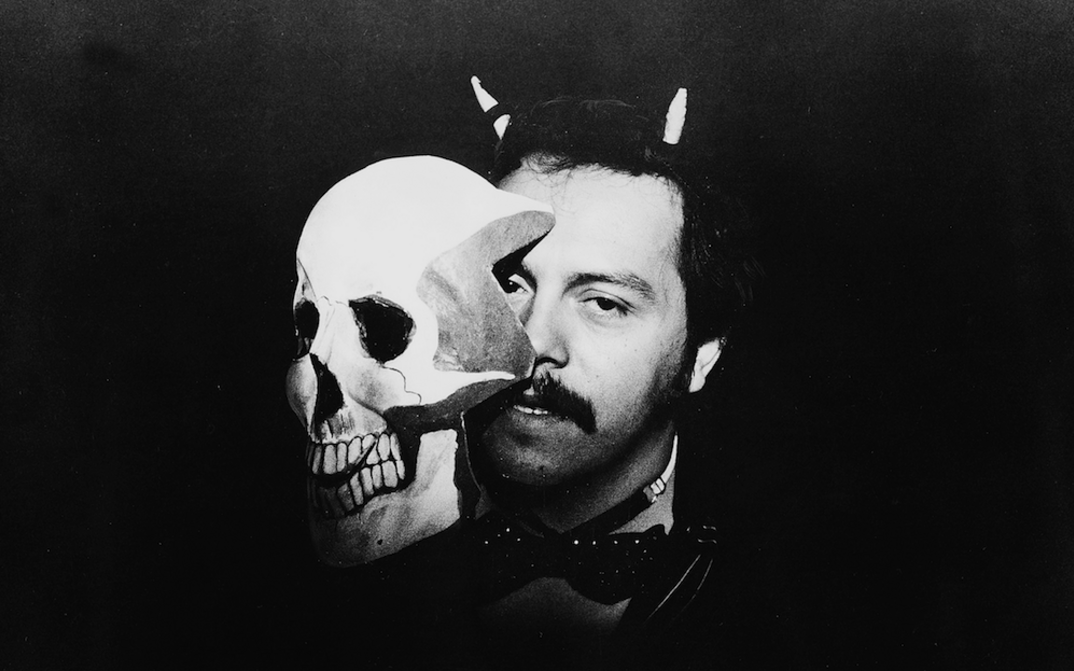 Film still from BLONDER TANGO: A man holds a skull mask in front of his face.