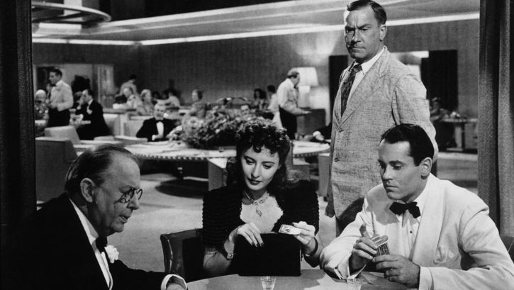Film still from THE LADY EVE: A woman and two men, all elegantly dressed, are playing cards.