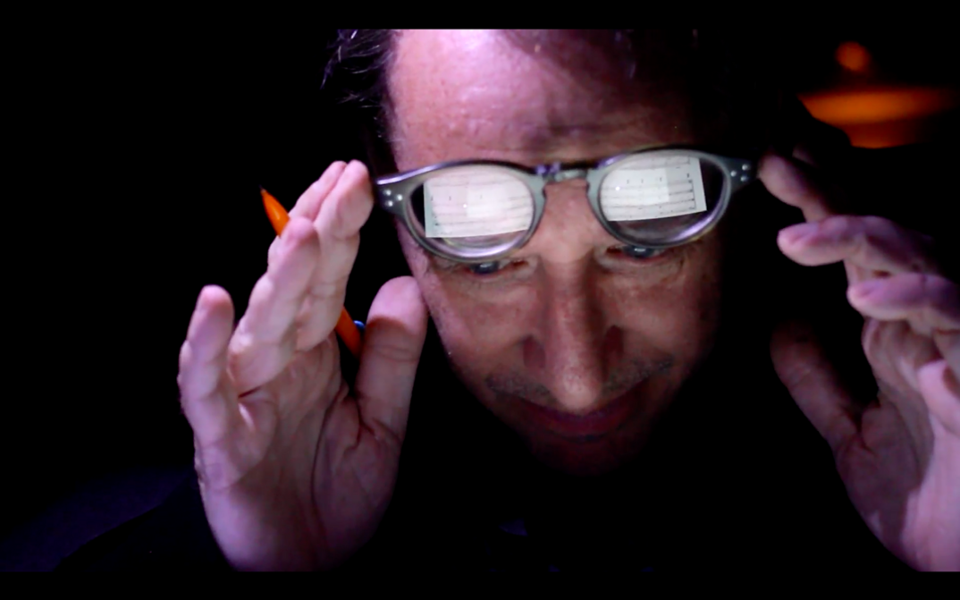 Filmstill aus ZORN. Nahaufnahme von John Zorn, in seinen Brillengläsern spiegeln sich Noten.