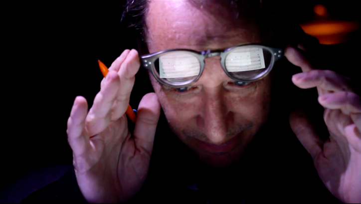 Filmstill aus ZORN. Nahaufnahme von John Zorn, in seinen Brillengläsern spiegeln sich Noten.