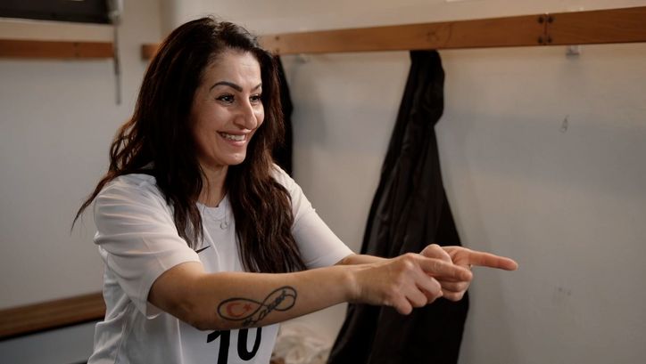 Filmstill aus SPIELERINNEN: Eine Frau in einem Fussballtrikot steht in einer Umkleidekabine und motiviert ihre Mitspielerinnen, die nicht im Bild sind.