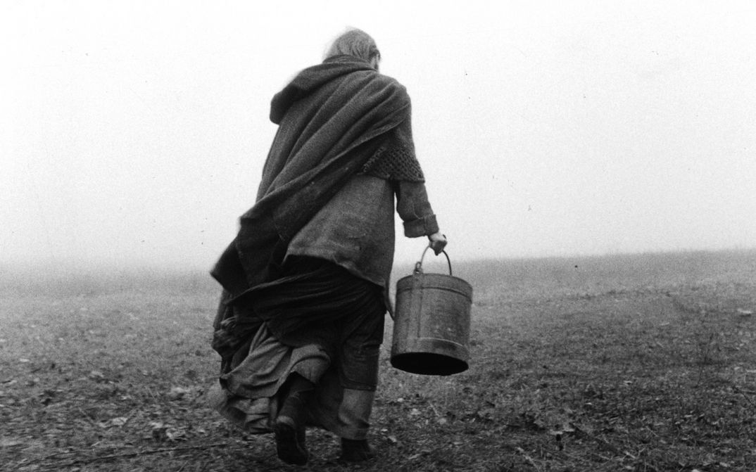 Filmstill aus DAS TURINER PFERD: Von hinten ist eine Person zu sehen, die über ein karges Feld läuft und einen Eimer trägt.