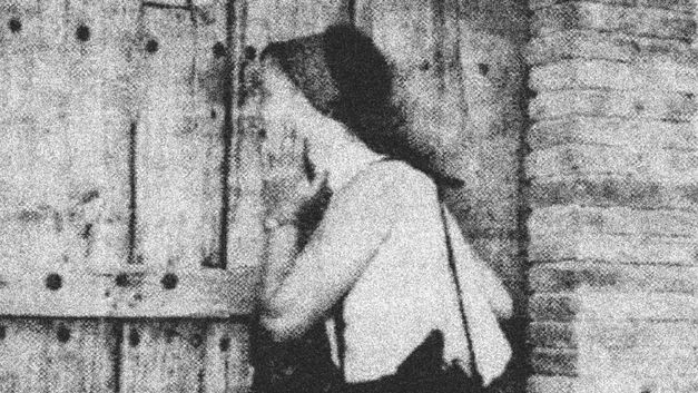 Filmstill aus dem Film „Exhibition“ von Mary Helena Clark. Eine Person an einer Holztür; das Bild ist schwarz-weiß und stark gekörnt.