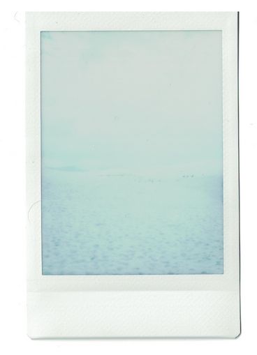 Polaroid of a light blue body of water, with the image overexposed and blurry.
