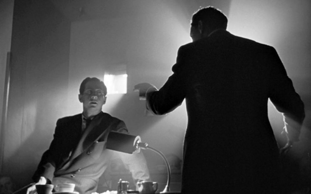Filmstill aus CITIZEN KANE: Zwei Männer argumentieren von zwei Seiten eines Schreibtisches. Der Raum ist dunkel, aber wird durch einfallendes Licht aus einem kleinen Fenster und einer Schreibtischlampe beleuchtet, so dass starke Kontraste entstehen.