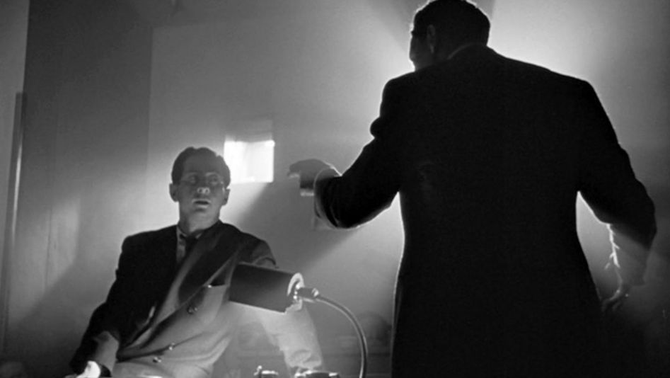 Filmstill aus CITIZEN KANE: Zwei Männer argumentieren von zwei Seiten eines Schreibtisches. Der Raum ist dunkel, aber wird durch einfallendes Licht aus einem kleinen Fenster und einer Schreibtischlampe beleuchtet, so dass starke Kontraste entstehen.