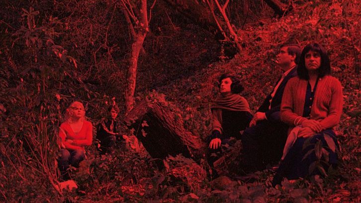 Filmstill aus MORRER COMO UM HOMEM: Ein rot eingefärbtes Bild einer Gruppe von Menschen, die in einem Wald sitzt.