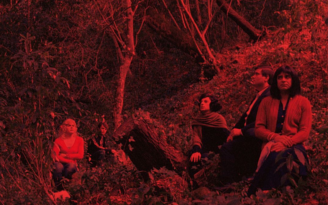 Filmstill aus MORRER COMO UM HOMEM: Ein rot eingefärbtes Bild einer Gruppe von Menschen, die in einem Wald sitzt.