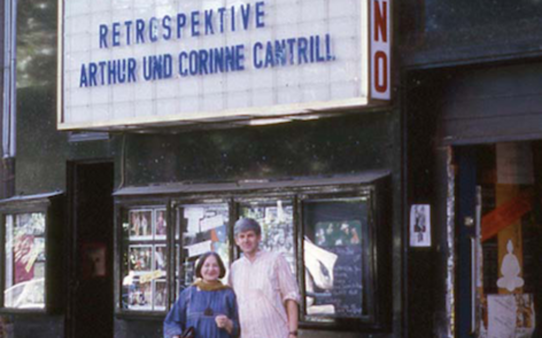Portrait of Arthur and Corinne Cantrill in front of the program display at the old Arsenal, which reads "Retrospective Arthur and Corinne Cantrill".