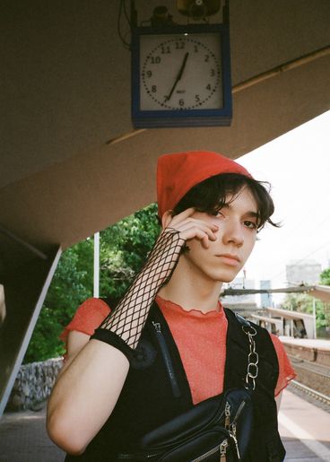 Youth with red scarf on his head stands at a railroad track, above him a clock