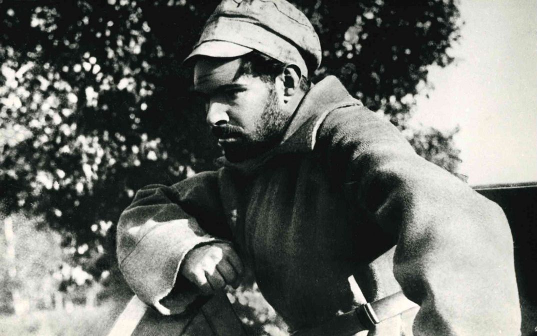 Film still from ARSENAL: A man in a coat and cap looks thoughtfully in front of him.