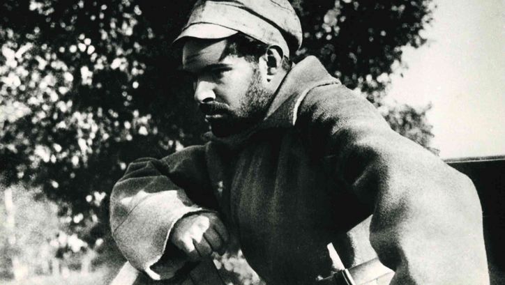 Film still from ARSENAL: A man in a coat and cap looks thoughtfully in front of him.