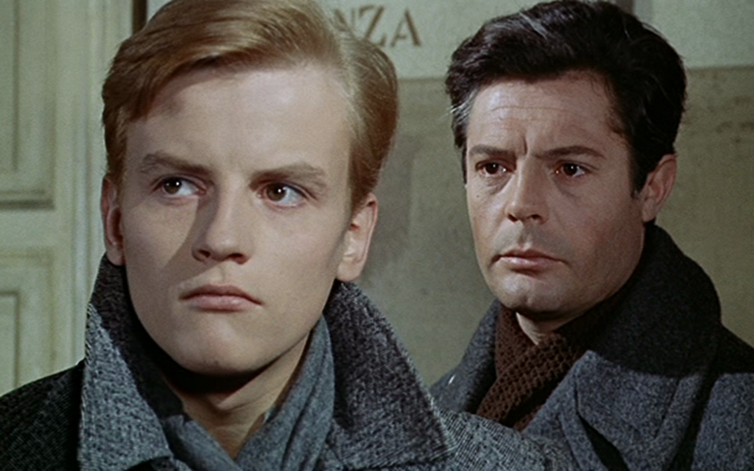Film still from CRONACA FAMILIARE. Two men in winter coats stand one behind the other, one of them is Marcello Mastroianni.