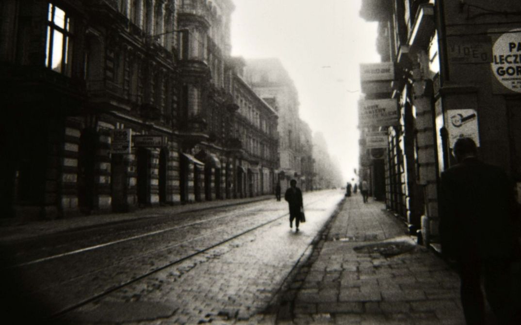 Film still from LODZ SYMPHONY: A gloomy, narrow street with a few people on it.