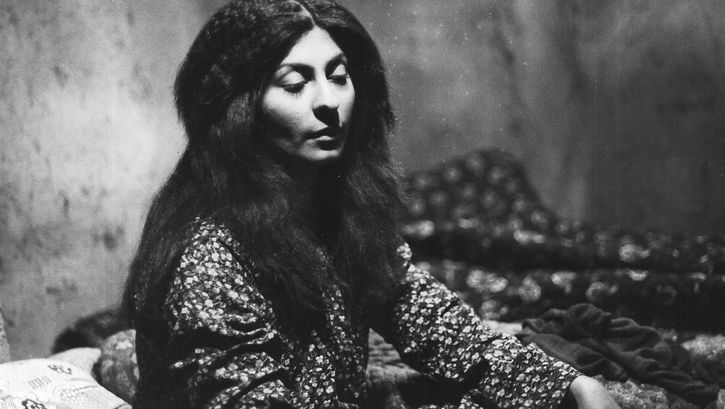 Film still from THE SEALED SOIL. A young woman with long hair sits in a room with half-closed eyes. 