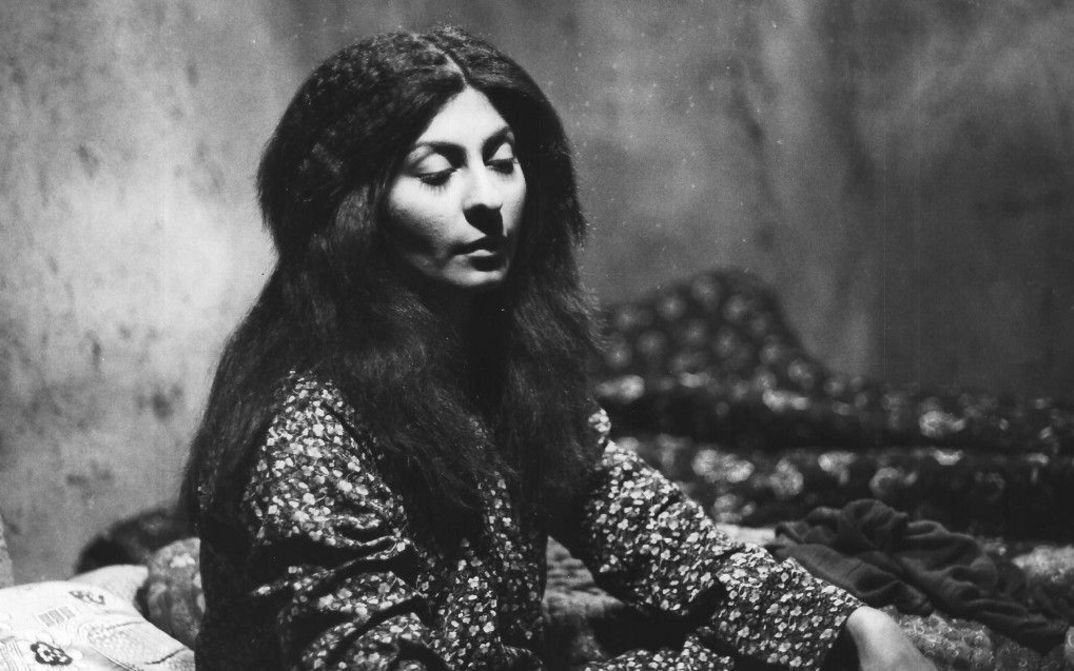 Film still from THE SEALED SOIL. A young woman with long hair sits in a room with half-closed eyes.